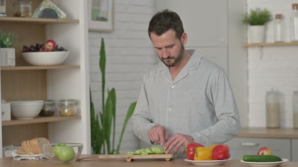 Здоровый молодой человек режет огурец на кухне — стоковое видео