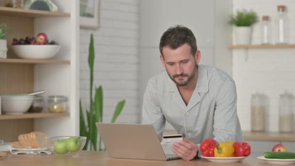 Человек делает онлайн оплату на ноутбуке в кухне — стоковое видео