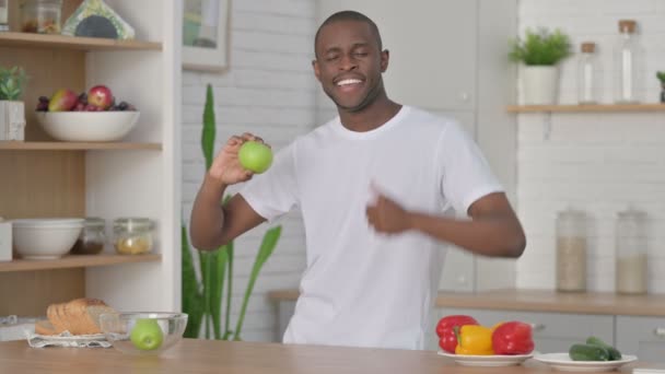 Спортивный африканский человек показывает пальчики вверх, держа Apple на кухне — стоковое видео