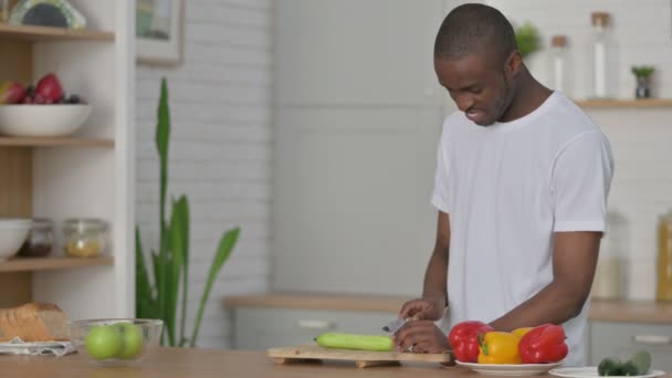 Gezonde Afrikaanse man snijden komkommer in keuken — Stockvideo
