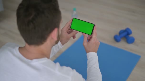 Visão traseira do homem olhando para o smartphone com tela chave Chroma no tapete de ioga — Vídeo de Stock