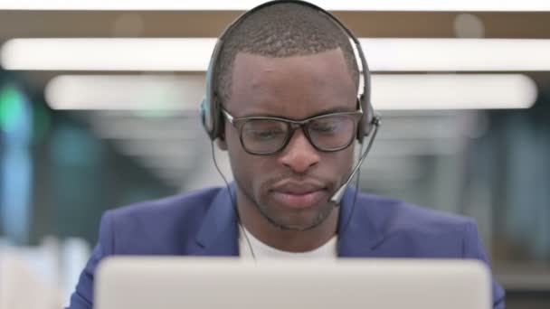 Портрет африканского бизнесмена с наушниками, работающего на ноутбуке — стоковое видео