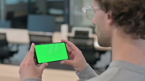 Вид сзади молодого предпринимателя, смотрящего на смартфон с хромированным экраном — стоковое видео
