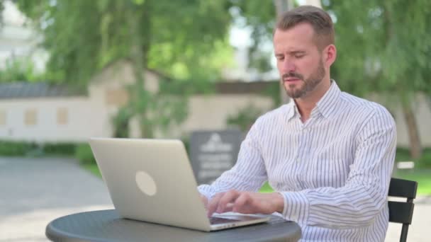 Mann mittleren Alters mit Laptop hat Kopfschmerzen in Outdoor-Café — Stockvideo