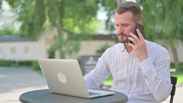 Mann mittleren Alters spricht in Outdoor-Café mit Smartphone — Stockvideo