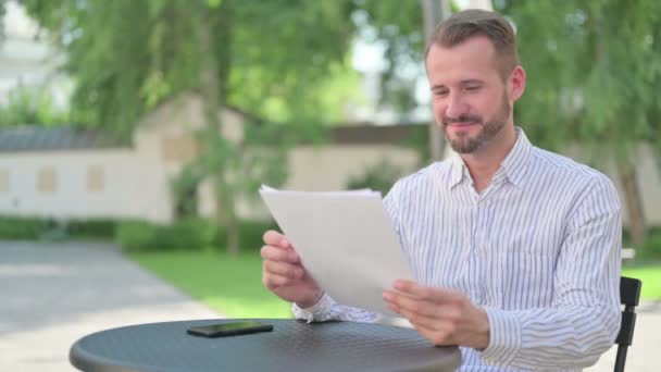 Medelålders man firar framgång när du läser dokument, utomhus — Stockvideo