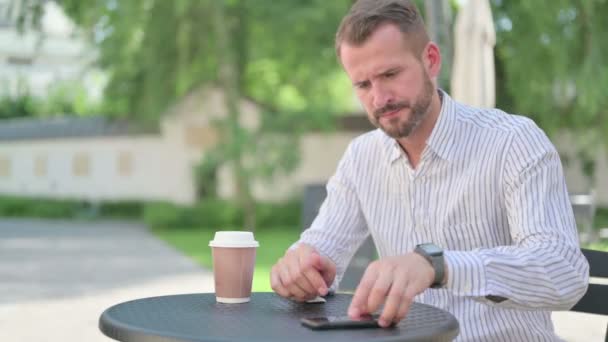 Hombre de mediana edad se siente enojado mientras espera en el café al aire libre — Vídeos de Stock