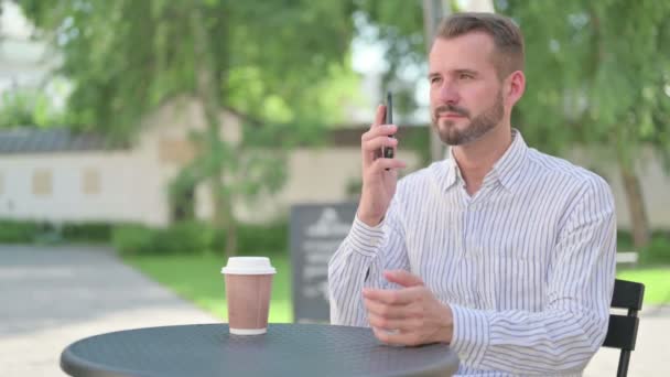 Medelålders man talar på smartphone i utomhus café — Stockvideo