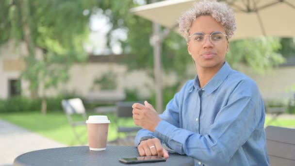 커피를 마시며 기다리는 젊은 아프리카 여자, 옥외 카페에서 시간을 확인하는 모습 — 비디오