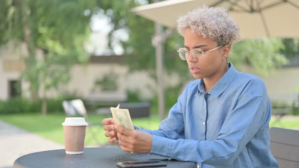 Jovem mulher africana sentindo-se triste enquanto conta dólares no café ao ar livre — Vídeo de Stock
