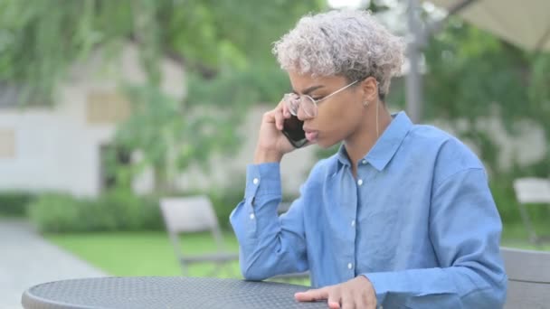 怒っている若いアフリカ人女性が屋外カフェで電話で話す — ストック動画