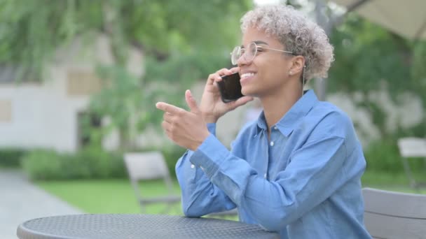 Mladá africká žena mluví na telefonu v venkovní kavárně — Stock video