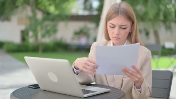 Jeune femme d'affaires avec ordinateur portable lecture de documents dans un café en plein air — Video