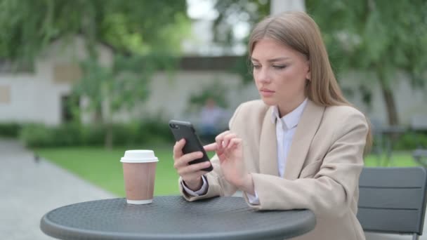 Νεαρή επιχειρηματίας αντιδρώντας στην απώλεια για Smartphone σε υπαίθριο καφέ — Αρχείο Βίντεο