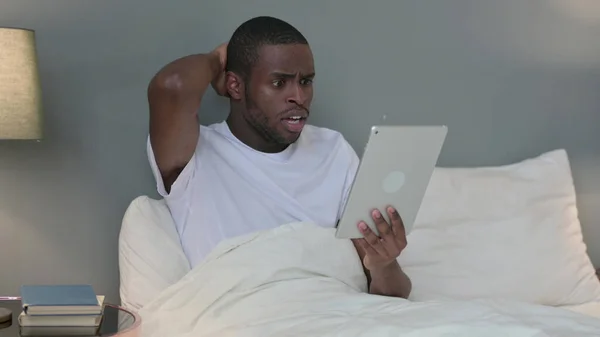 Hombre joven africano reaccionando a la pérdida en la tableta en la cama —  Fotos de Stock