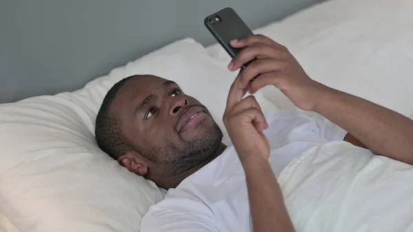 Uso de Smartphone por Jovem Africano Deitado na Cama — Fotografia de Stock