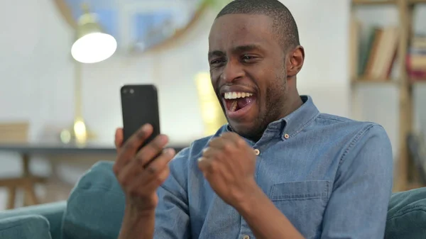Hombre joven africano celebrando en el Smartphone en casa —  Fotos de Stock