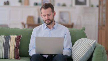 Dizüstü bilgisayarda çalışırken uyuyan yorgun genç adam, koltukta oturan... 