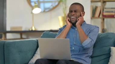 Dizüstü bilgisayarı olan genç Afrikalı adam koltukta baş ağrısı çekiyor. 