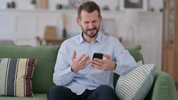 Jonge man reageert op verlies op Smartphone op Sofa — Stockfoto