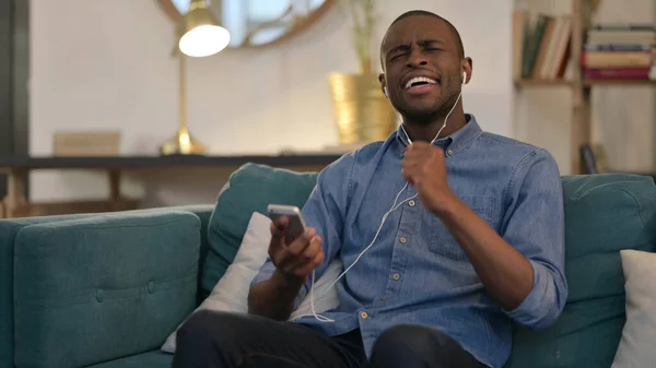 Junger Afrikaner hört auf Sofa Musik auf Smartphone — Stockfoto