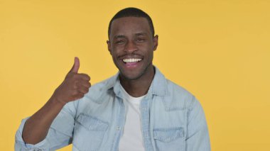Başparmakları havada, sarı arkaplanı olan genç Afrikalı. 