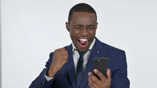 Empresario africano animando el éxito en Smartphone, fondo blanco —  Fotos de Stock