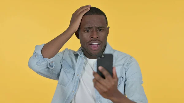 Joven pérdida de hombre africano en Smartphone, Fondo amarillo —  Fotos de Stock