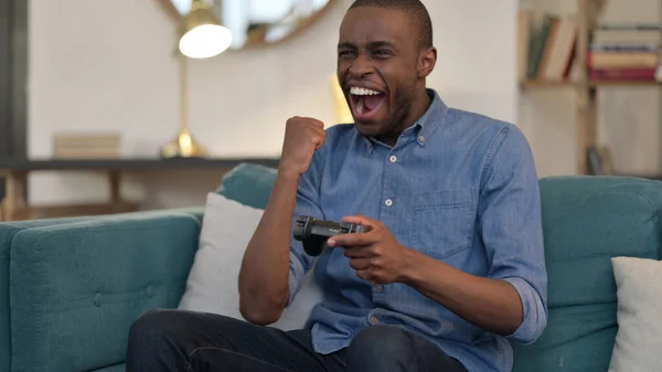 Young African Man Celebrating Success on Video Game on Sofa — Stock Photo, Image