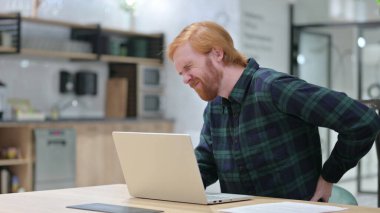 Kafede dizüstü bilgisayar kullanan sırt ağrısı olan kızıl saçlı adam. 