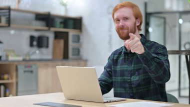 Bilgisayarlı kızıl saçlı adam kamerayı işaret ediyor. 