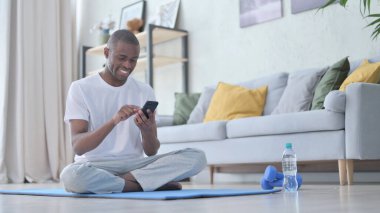 Afrikalı Adam Yoga Mat 'te akıllı telefon kullanıyor.