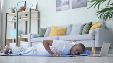 Evde yoga yaparken yorgun Afrikalı adam şınav çekiyor.