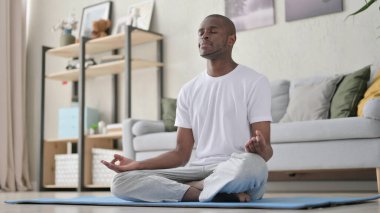 African Man Meditating on Yoga Mat at Home clipart