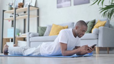 Akıllı telefon kullanan Afrikalı adam Yoga Mat 'in üzerinde yatıyor 