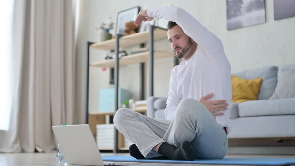 Felnőtt férfi jógát tanít videohívásra, miközben a jóga matracon ül — Stock Fotó