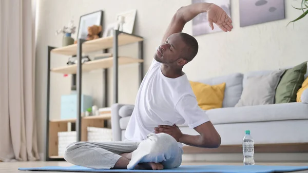 Afrikai férfi nyújtózkodik jóga matracon otthon — Stock Fotó