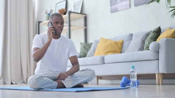 Afrikai férfi beszél telefonon jóga matracon otthon — Stock Fotó