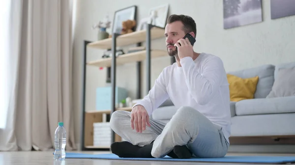 Felnőtt férfi beszél telefonon jóga matracon otthon — Stock Fotó