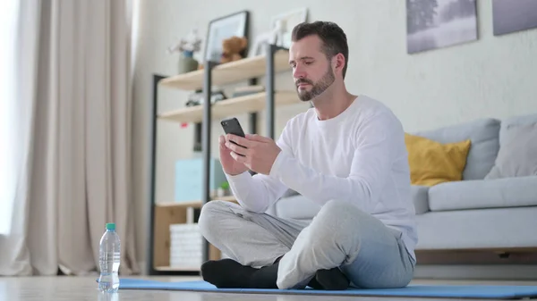 Hombre adulto maduro usando Smartphone en Yoga Mat en casa —  Fotos de Stock