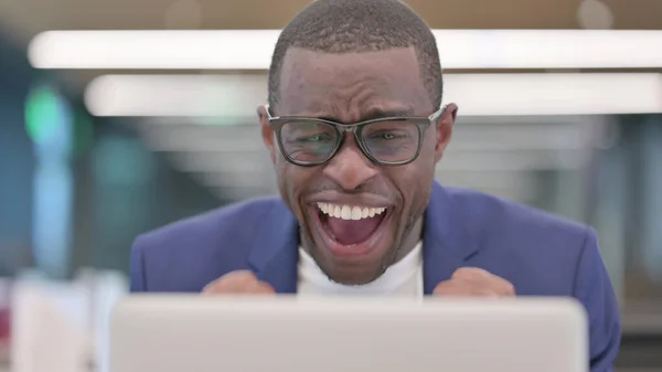 Framgångsrik ung afrikansk affärsman firar på laptop på jobbet — Stockfoto