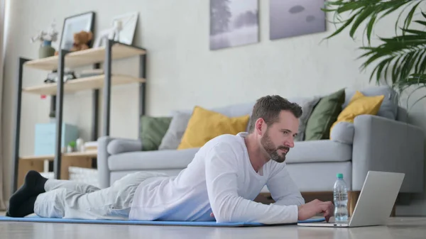 Hombre adulto maduro usando el ordenador portátil mientras que pone en la estera del yoga en el país —  Fotos de Stock