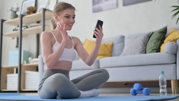 Mujer hablando en videollamada en Smartphone mientras está sentada en Yoga Mat —  Fotos de Stock