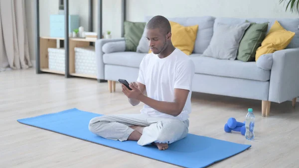 Afrikai férfi használja okostelefon jóga matrac otthon — Stock Fotó