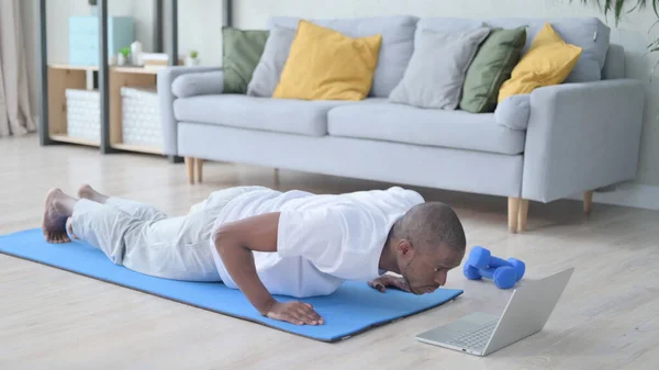 Hombre africano mirando el ordenador portátil mientras hace flexiones en la estera de yoga — Foto de Stock