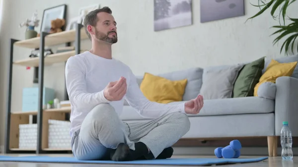 Peaceful Mature Adult Man Meditating on Yoga Mat at Home