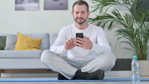 Hombre adulto maduro usando Smartphone en Yoga Mat en casa —  Fotos de Stock