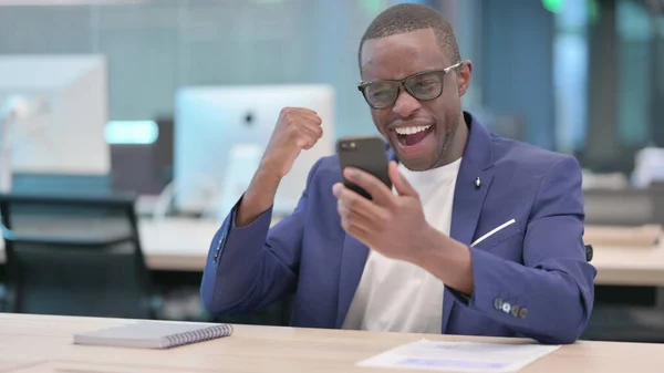 年轻的非洲商人在办公室用智能手机庆祝成功 — 图库照片
