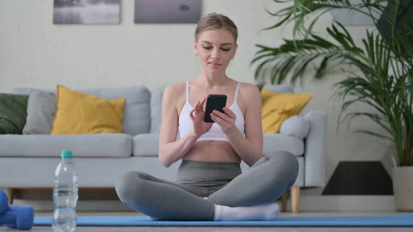 Mujer usando Smartphone en Estera de Yoga en Casa —  Fotos de Stock