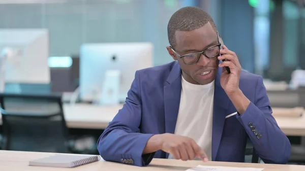 Joven empresario africano hablando por teléfono en el trabajo —  Fotos de Stock